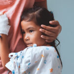 Child in a hospital gown embraces her parent.