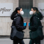 A woman walks past a Pfizer sign.