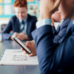 A teenager in a classroom wearing a school uniform and looking at smartphone